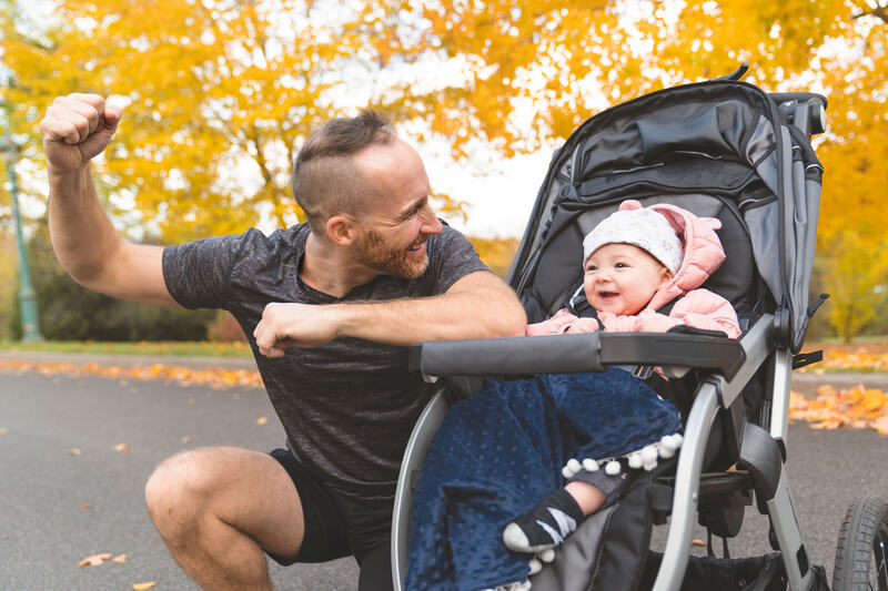 man with her daughter standing in jogging stroller outside in autumn nature